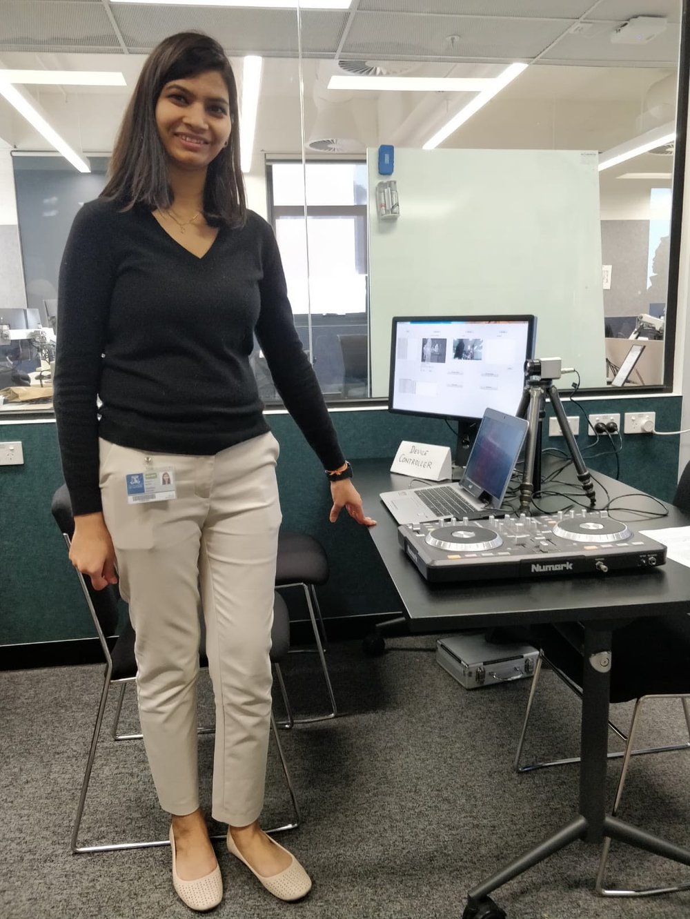 Namrata standing beside her PhD system: a laptop, a thermal camera on a tripod, and a controller on a desk.